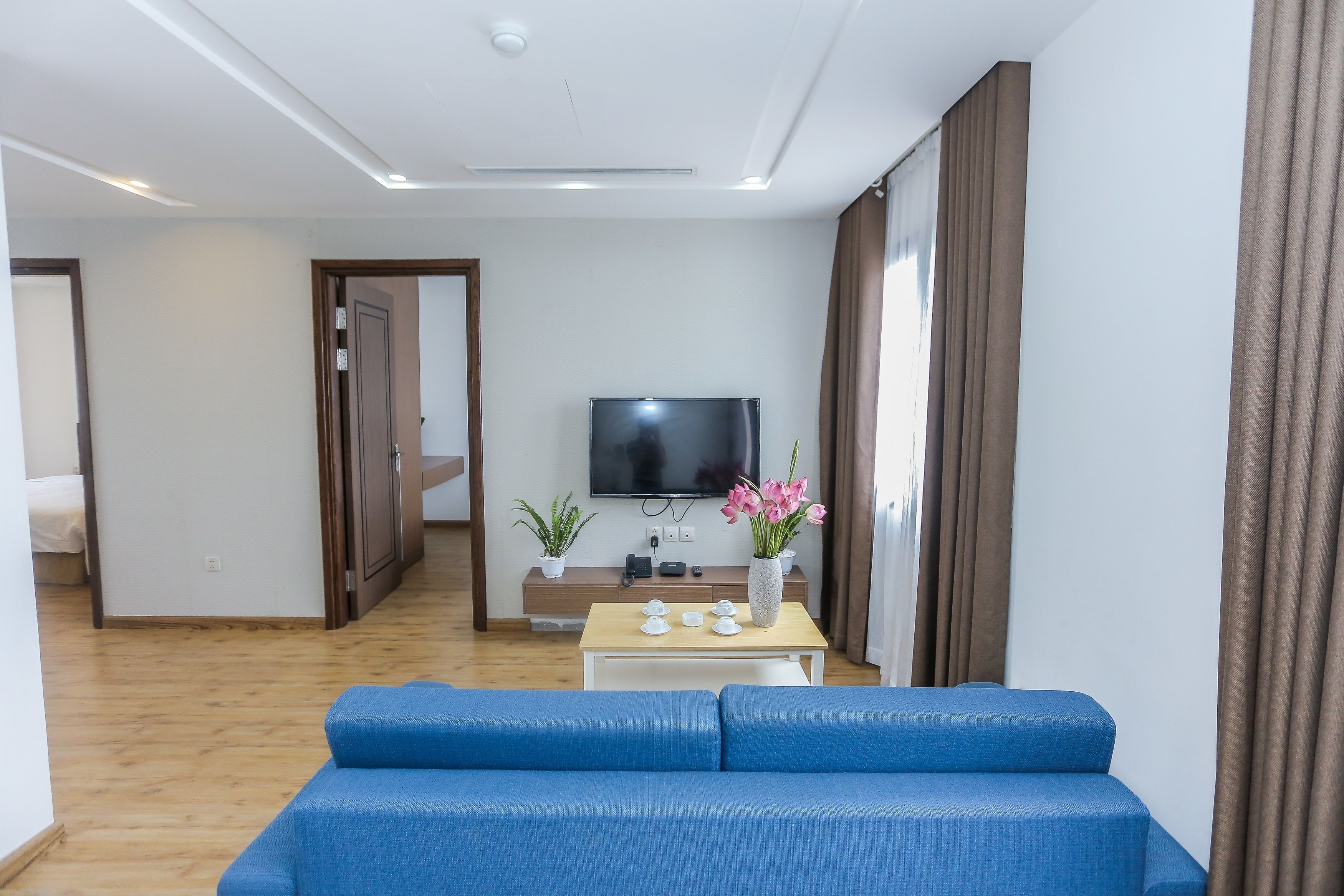 Una sala de estar moderna con un sofá azul, un televisor de pantalla plana, una mesa de centro y un jarrón con flores.