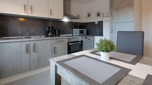 Eine moderne Küche mit integriertem Mikrowellenherd, Kaffeemaschine und Backofen. Ein Esstisch mit Topfpflanze und geometrischem Platzsetzer.