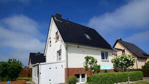 Ein zweistöckiges Haus mit geneigtem Dach, einer Garage und einem kleinen Vorgarten mit einer Hecke und einem Baum.