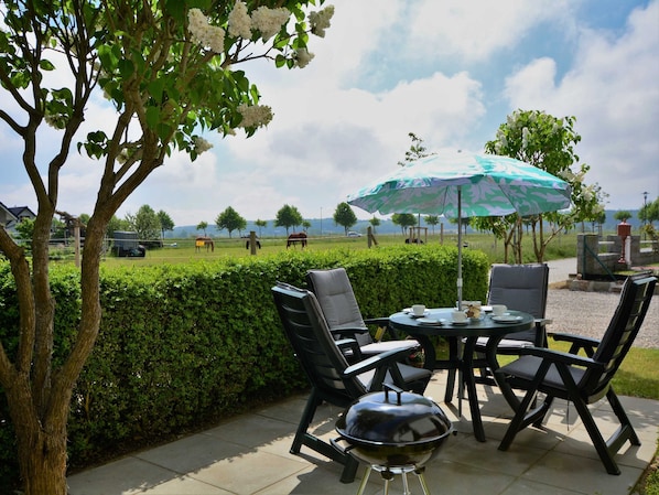 Une terrasse extérieure avec un barbecue, des chaises et un parasol.
