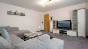 Ein modernes Wohnzimmer mit grauen Sofas, einem Flachbildfernseher, einem Couchtisch und einer Vitrine mit Dekoration.