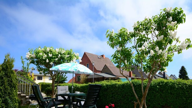 Ein Terrassenbereich im Freien mit Tisch und Stühlen, einem blau-weißen Sonnenschirm und Blick auf Häuser im Hintergrund.