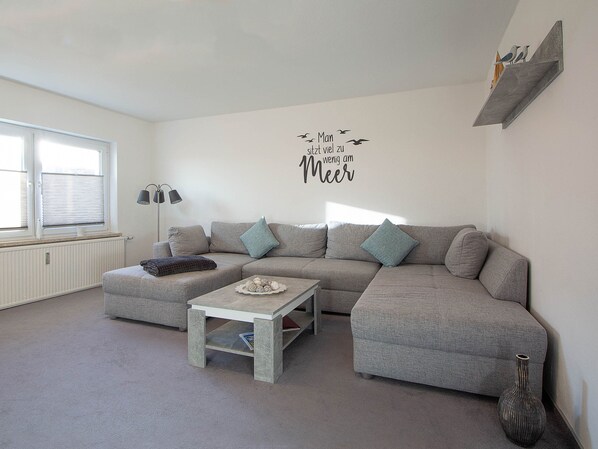 Een moderne woonkamer met een grijze modulaire bank, een klein bijzettafeltje en een decoratief wandbord.