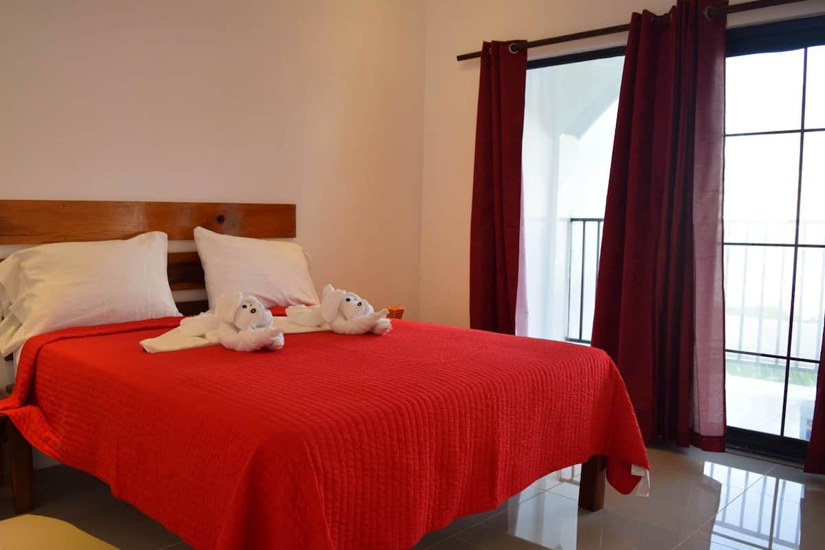 A hotel room with a large bed, red bedding, white pillows, and two plush dog-shaped pillows.