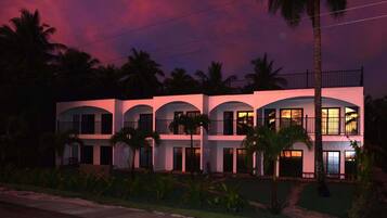 Un edificio de varios pisos con balcones y ventanas de arco, rodeado de palmeras.