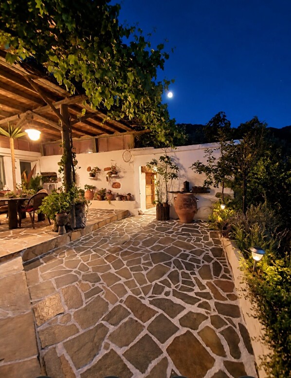 A stone-paved courtyard with a pergola, potted plants, and a white wall with hanging decorations.