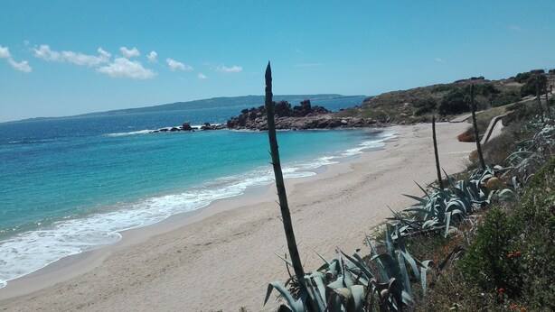 A beach with clear blue water, sandy shore, and rocky outcrops. - Vacation in the House of Dreams (Portoscuso)