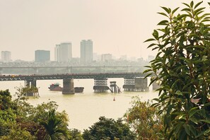 A river with a bridge, boats, and a city skyline in the background. - Lucky Budda Inn Villa (Hanoi)