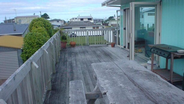 Eine Holzdielen-Terrasse mit Picknicktischen, einem Grill und einer Glastür zu einem überdachten Bereich.