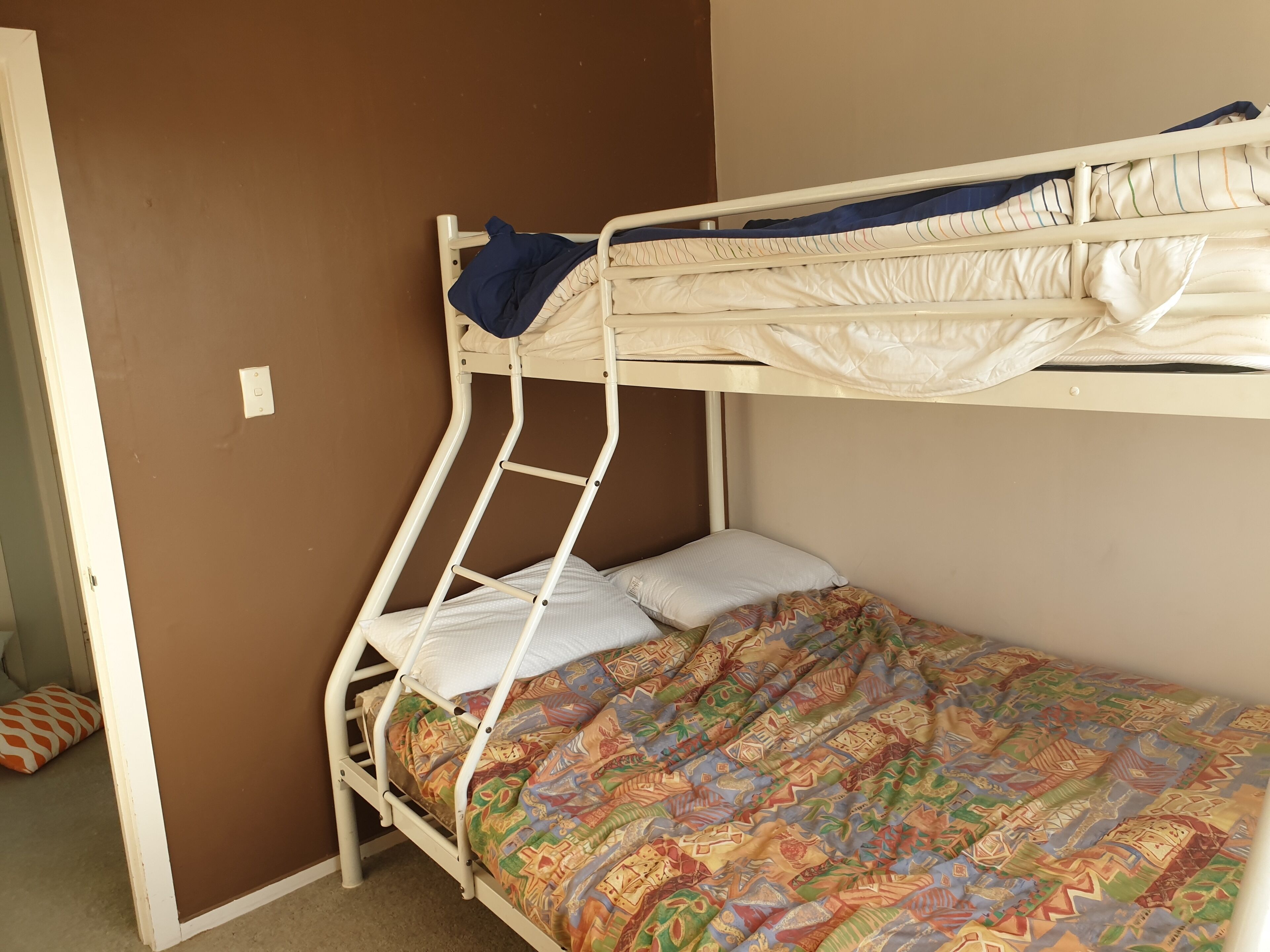 A bunk bed with a colorful patterned bedspread, a white mattress, and a blue blanket.