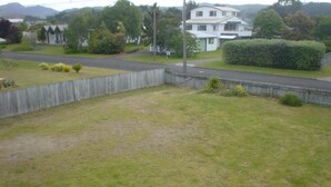 Ein Rasen mit Holzzaun, eine Straße und Häuser im Hintergrund.