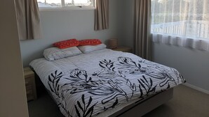 Ein Schlafzimmer mit einem Bett, zwei Nachttischen, einem Fenster mit Vorhängen und Blick ins Freie.