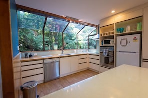 A modern kitchen with a large window, built-in appliances, and a view of greenery. - Retreat on the Ridge - Lake Ōkareka, Sleeps 8 (Rotorua)