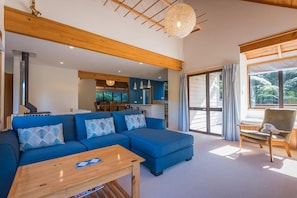 A modern living room with a sectional sofa, a wooden coffee table, and a dining area in the background. - Retreat on the Ridge - Lake Ōkareka, Sleeps 8 (Rotorua)