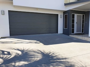 Adjacent to a house with a white exterior, this garage features a closed roller door and a small entrance with a glass door and metal gate.