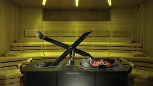 A sauna with benches, a central table with a bowl of fruits, and overhead lighting. - Marriott Park hotel Rome (Lazio)