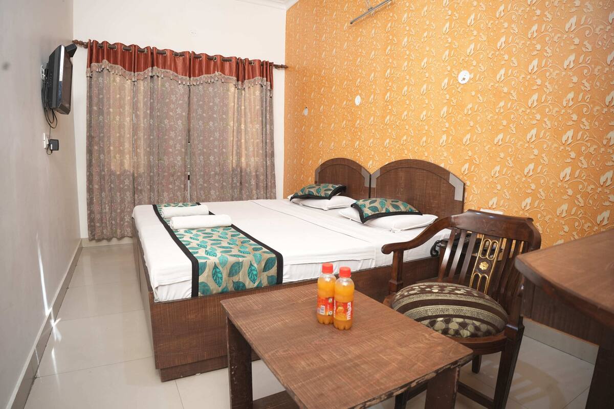 A hotel room with a bed, a wooden table, two chairs, and a television mounted on the wall.