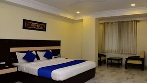 A hotel room with a large bed, a nightstand, a chair, a small table, and a window with curtains. - Hotel Holiday Comfort - 800 mts from Jallianwala Bagh, Amritsar (Amritsar)