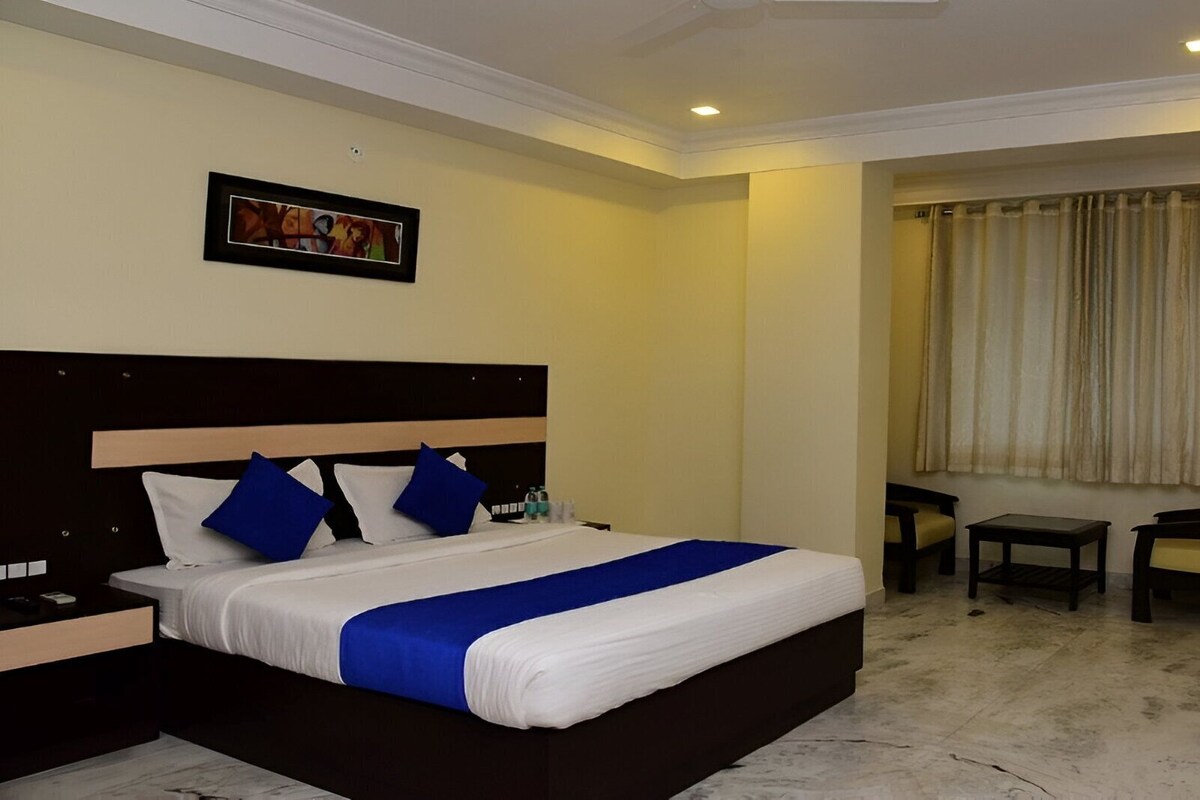 Ein Hotelzimmer mit einem großen Bett, einem Nachttisch, einem Sessel, einem kleinen Tisch und einem Fenster mit Vorhängen.