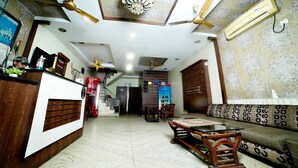 A spacious living area with a wooden reception desk, a sofa, a coffee table, and a ceiling fan. - Hotel Holiday Comfort - 800 mts from Jallianwala Bagh, Amritsar (Amritsar)