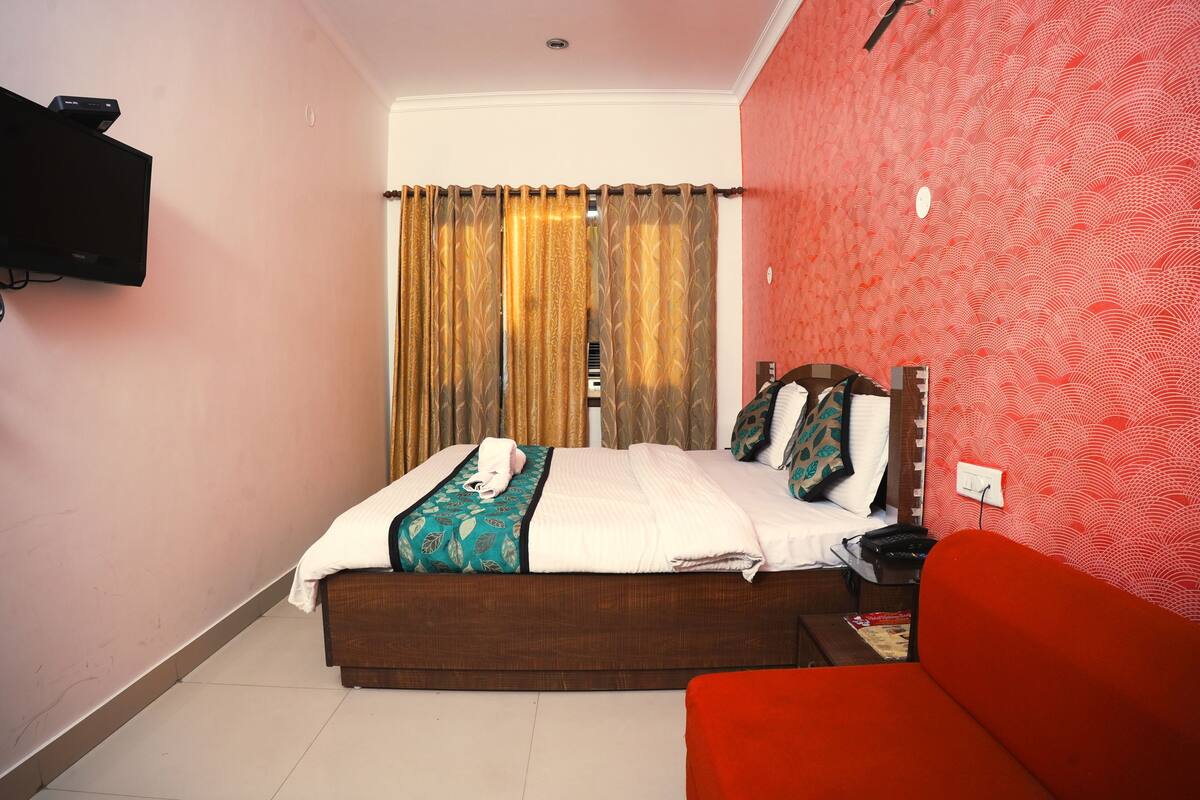 A hotel room with a bed, a red sofa, a television mounted on the wall, and a patterned wall.