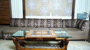 A living room with a glass-top coffee table, patterned sofa, and a decorative wall hanging. - Hotel Holiday Comfort - 800 mts from Jallianwala Bagh, Amritsar (Amritsar)