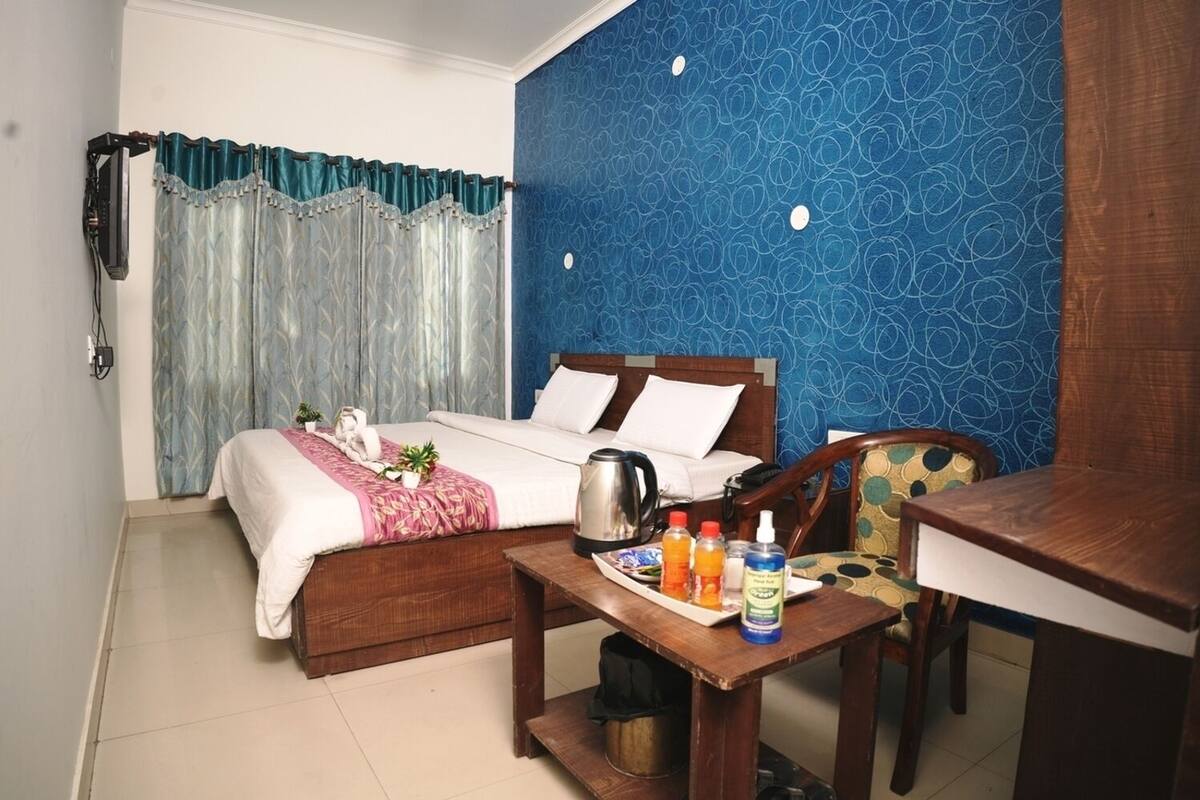 A hotel room with two beds, a wooden table with breakfast items, a coffee pot, and a wall with a blue pattern.