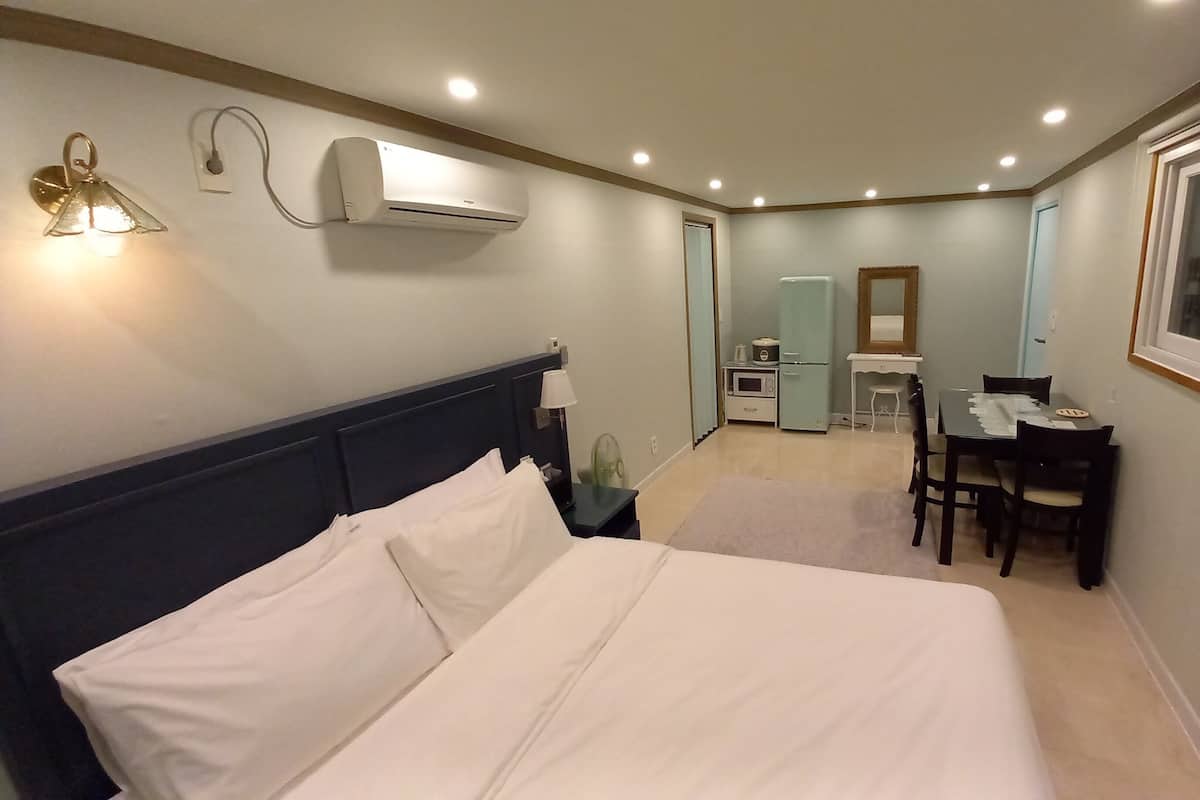 A hotel room with a bed, a desk, a chair, a small kitchenette, and a window.