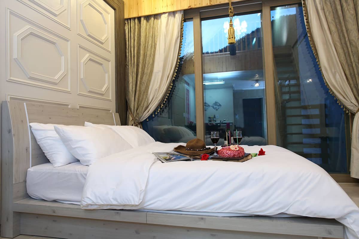 A bed with white bedding, a hat, a rose, and a bottle of wine on a windowsill.