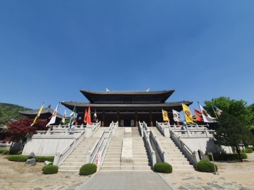 A traditional building with a tiled roof, multiple steps leading up to the entrance, and several flags at the top.