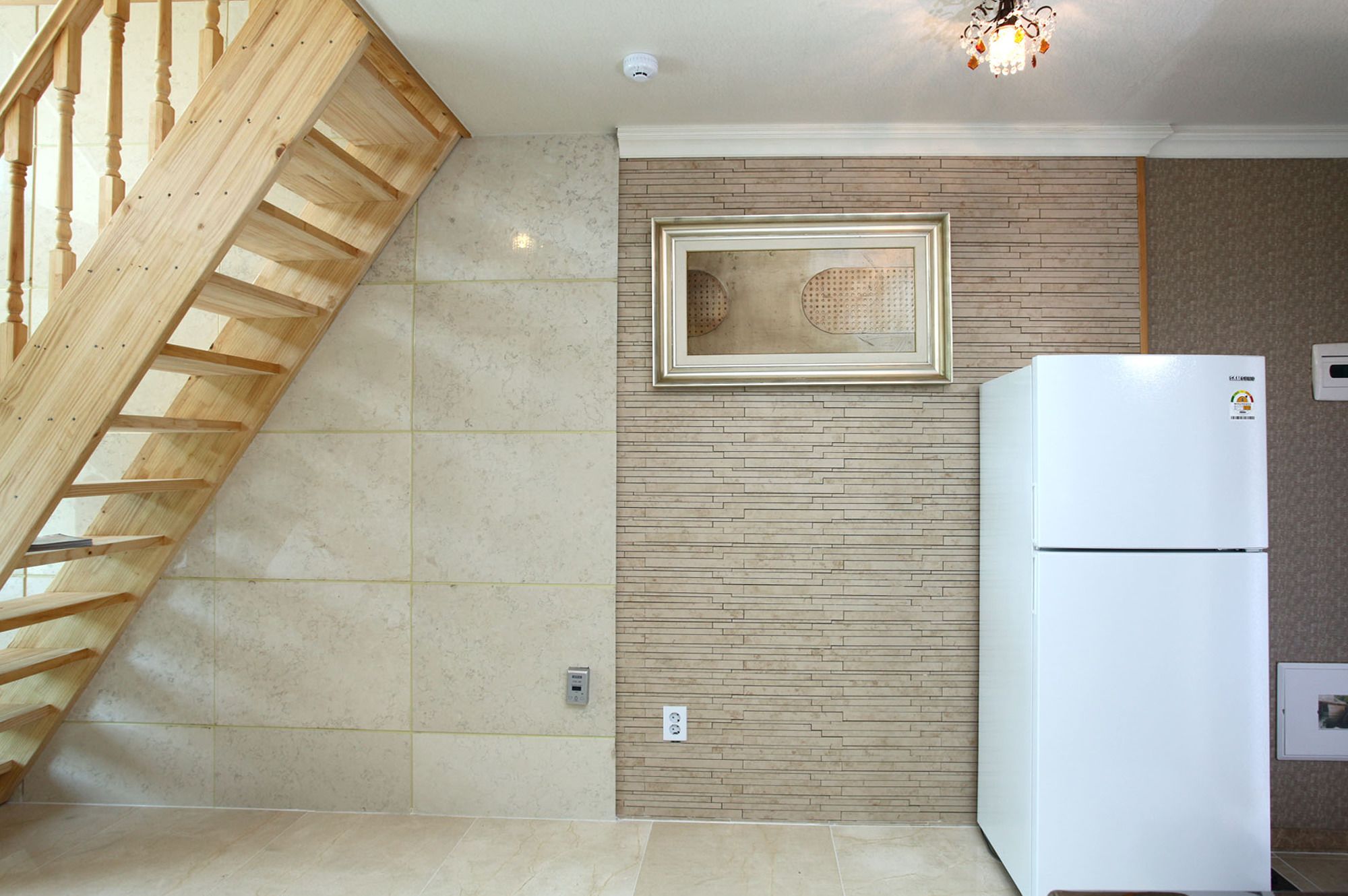 A kitchen with a wooden staircase, a white refrigerator, and a wall-mounted light fixture.