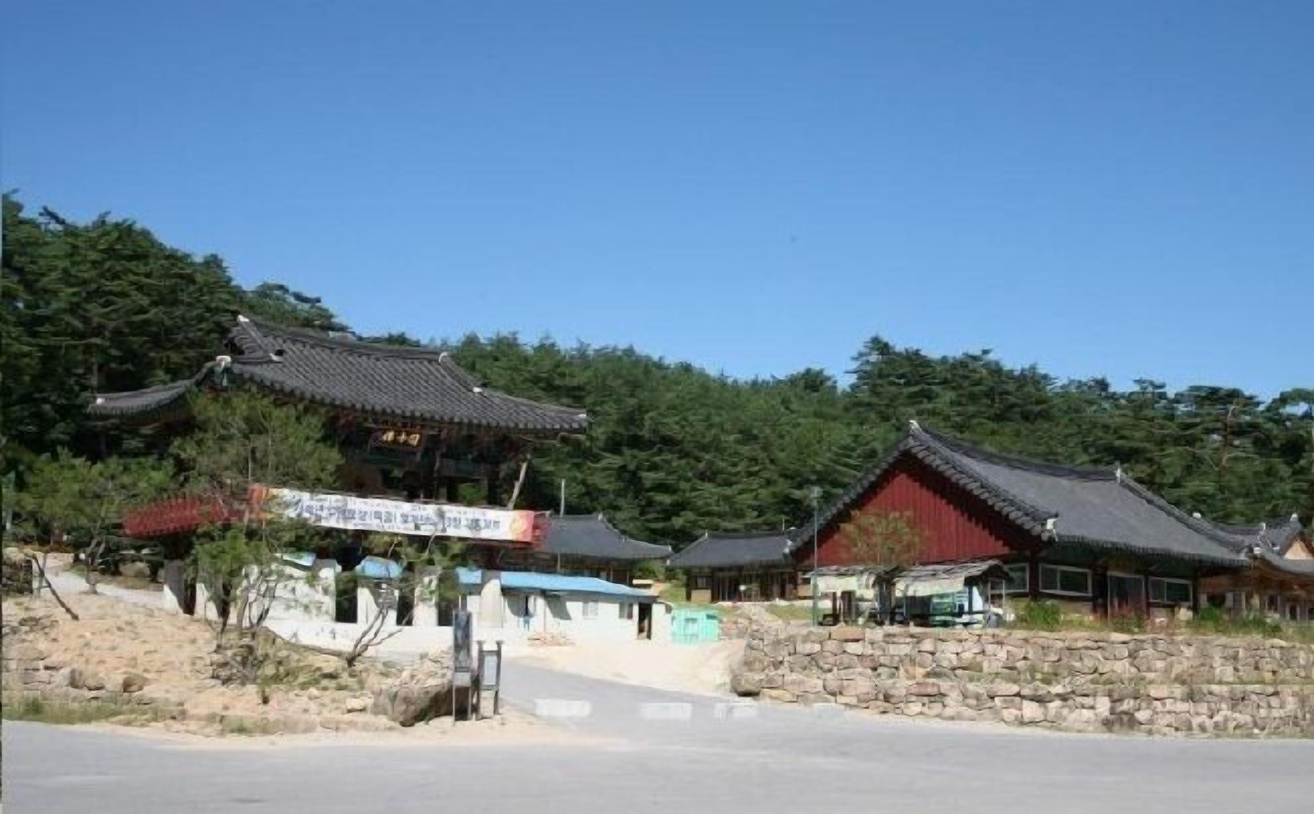 Un edificio tradicional coreano con tejado de tejas, rodeado de follaje y un muro de piedra.