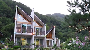 Un edificio moderno de dos pisos con un balcón, rodeado por un jardín ajardinado con diversas plantas y flores.