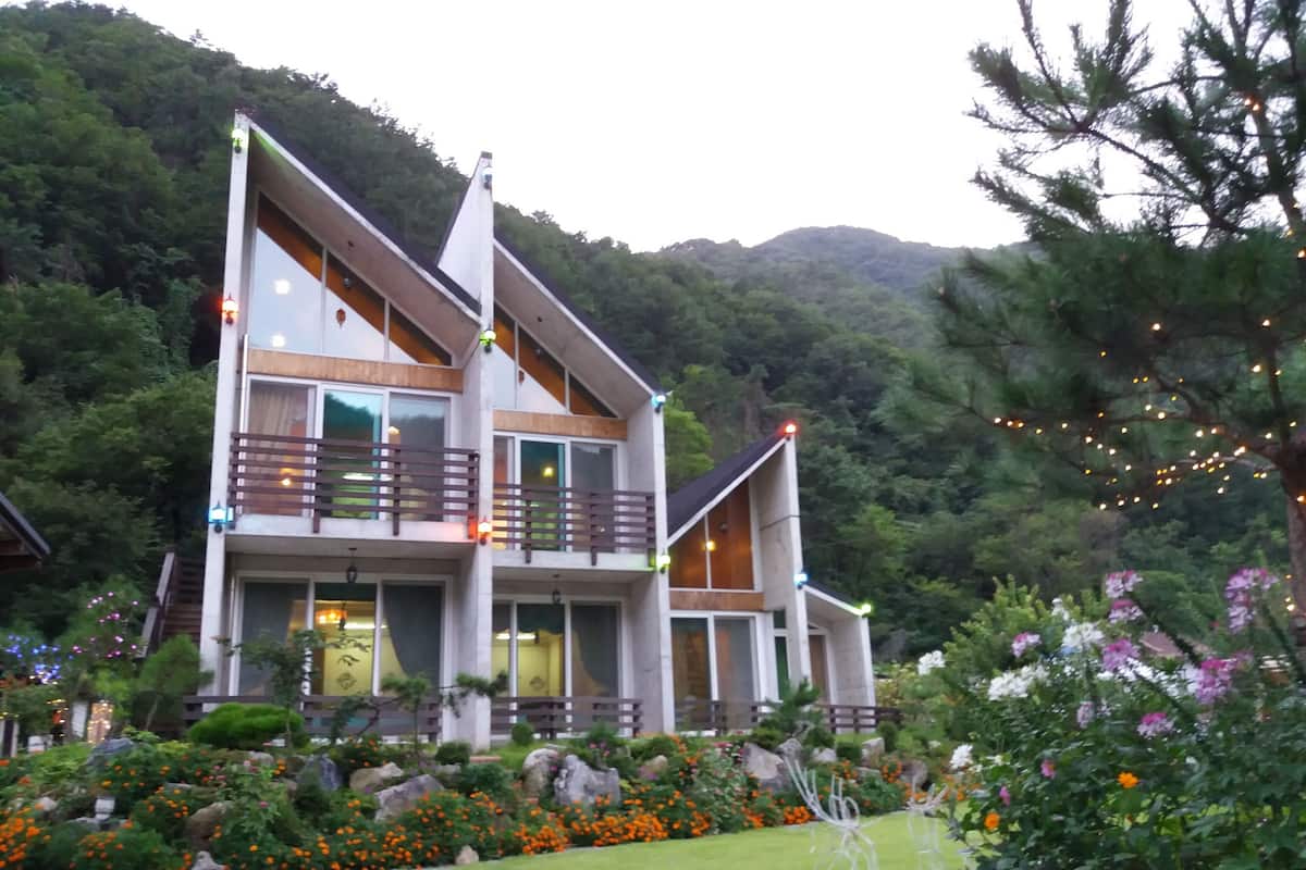 A modern two-story building with a balcony, surrounded by a landscaped garden with various plants and flowers.