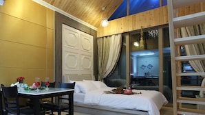 Un dormitorio con una cama, una mesa con sillas, un ventanal con cortinas y techo de madera.