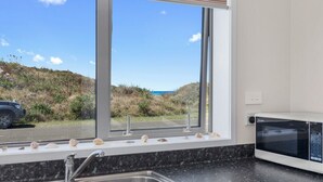 Uma cozinha com uma janela ampla, uma pia, um micro-ondas e vista para a praia.
