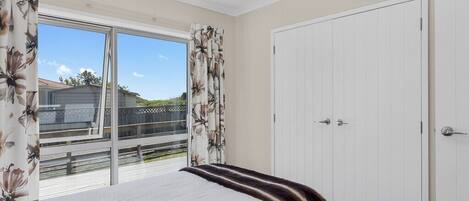 A bedroom with a large bed, a sliding glass door to a balcony, and a white wardrobe.
