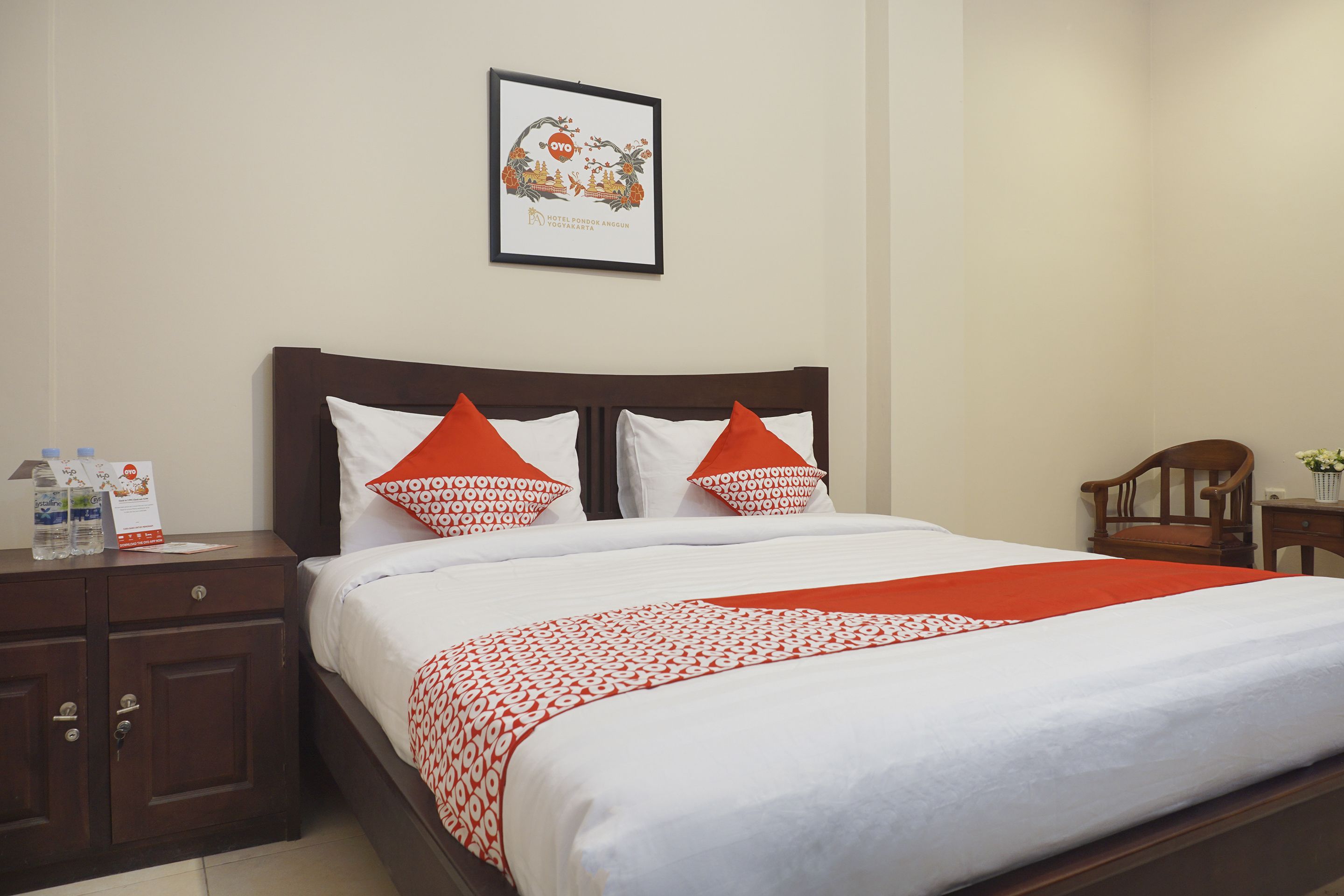 A neatly made bed with white and red bedding, a framed picture on the wall, and a wooden nightstand with a bottle and a small item on it.