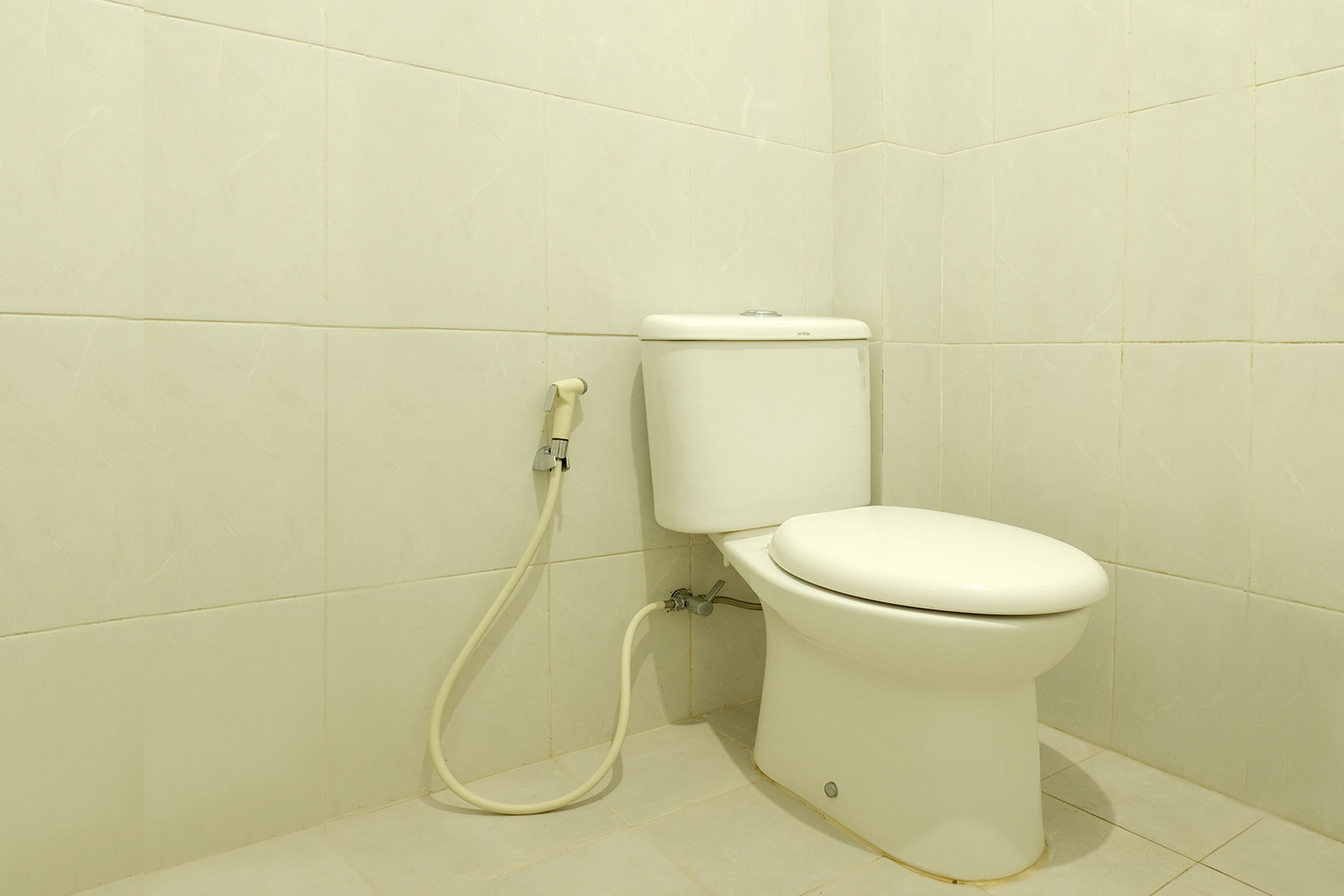 A toilet with a bidet attachment in a bathroom with white tiled walls and floor.