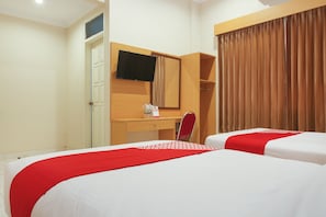 A hotel room with two beds, a desk, a chair, a TV, and a window with curtains.
