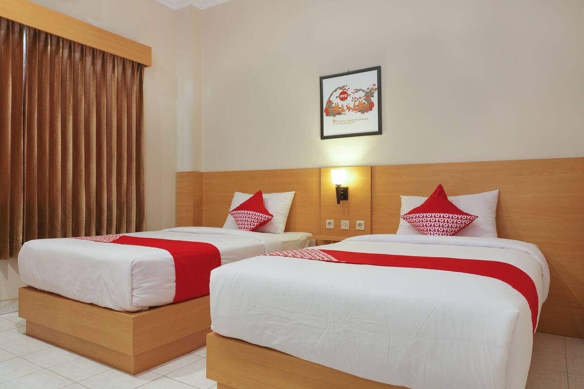 Une chambre d’hôtel avec deux lits, chacun agrémenté de draps blancs et de touches de couleur rouge, d’une tête de lit en bois et d’un tableau encadré au mur.