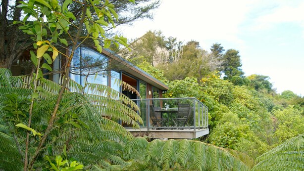 Una casa moderna con un balcón de vidrio rodeada de abundante vegetación.