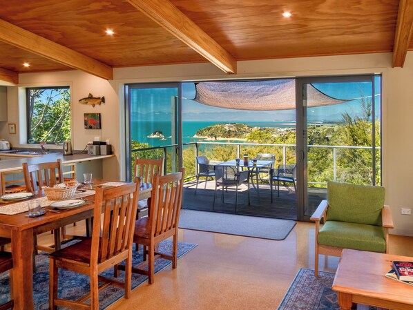 Un comedor con vista al mar, una cocina con un lavaplatos y un tostador, y un balcón con mobiliario exterior.
