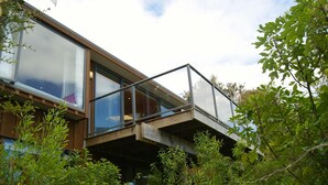 Un edificio moderno con balcón de vidrio, rodeado de abundante vegetación.
