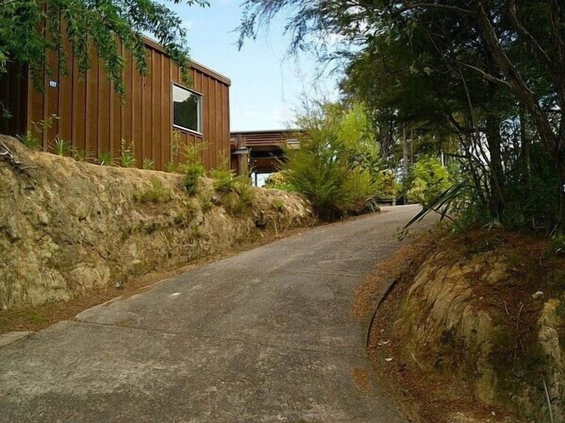A narrow road flanked by a wooden building with a large window and a stone retaining wall.