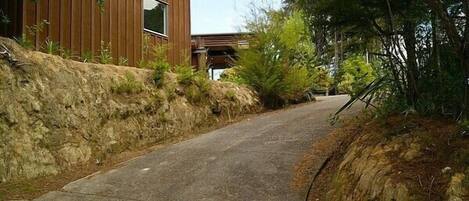 A narrow road flanked by a wooden building with a large window and a stone retaining wall.