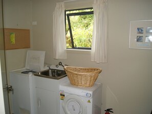 Een wasruimte met een wasmachine, een wasbak en een raam met gordijnen.
