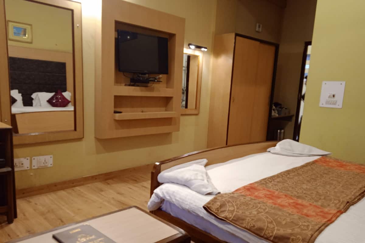 Una habitación de hotel con cama, televisión, aparador de madera y mesita de noche con un libro.