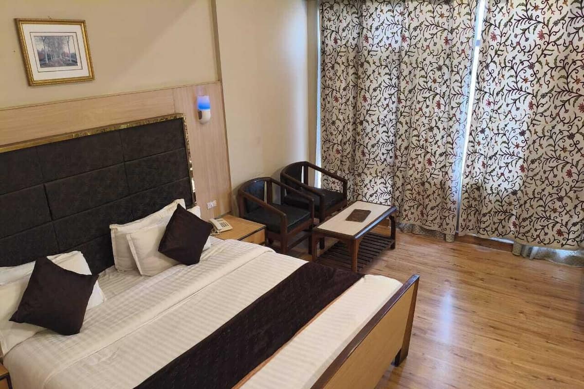 Una habitación de hotel con una cama grande, un escritorio, una silla y un ventanal con cortinas estampadas.