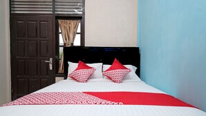 Una cama con ropa de cama blanca y roja, una colcha de cuadros rojos y blancos, y dos almohadas rojas con un diseño blanco.